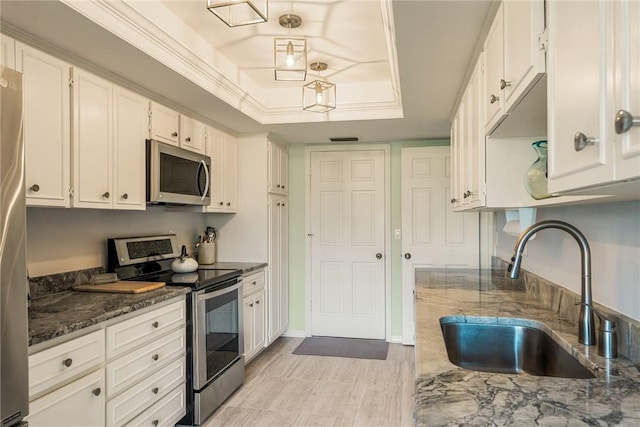 kitchen with sink, dark stone countertops, appliances with stainless steel finishes, a tray ceiling, and white cabinets