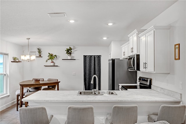 kitchen with white cabinetry, sink, stainless steel appliances, kitchen peninsula, and pendant lighting