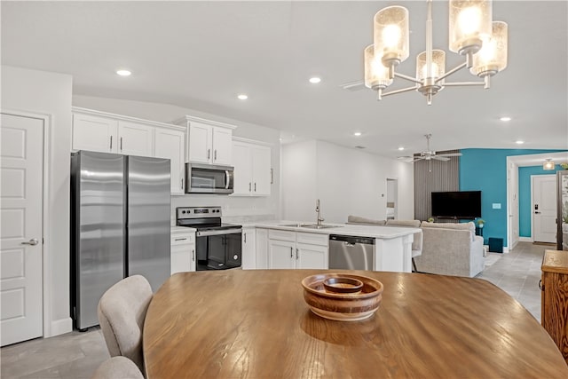 kitchen with white cabinetry, sink, stainless steel appliances, pendant lighting, and ceiling fan with notable chandelier