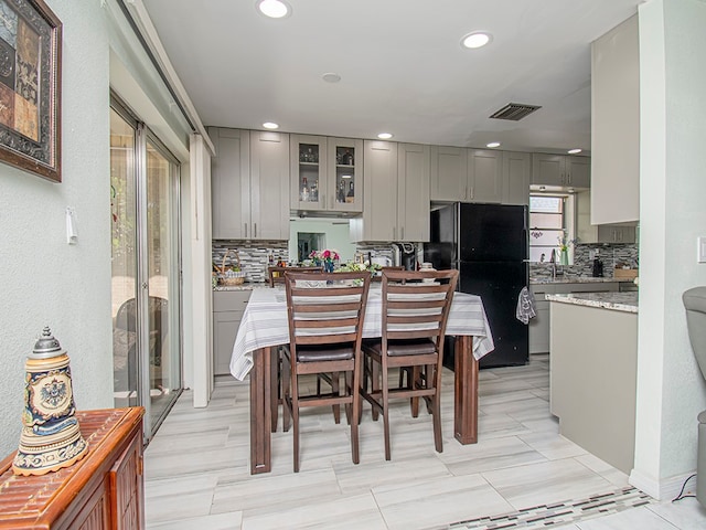 kitchen featuring light stone countertops, gray cabinetry, black fridge, and backsplash