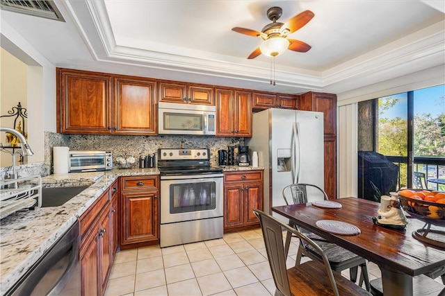 kitchen with light stone counters, light tile patterned floors, a tray ceiling, and stainless steel appliances