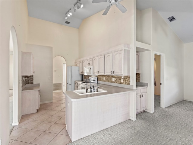 kitchen with kitchen peninsula, high vaulted ceiling, light tile patterned flooring, white cabinetry, and white appliances