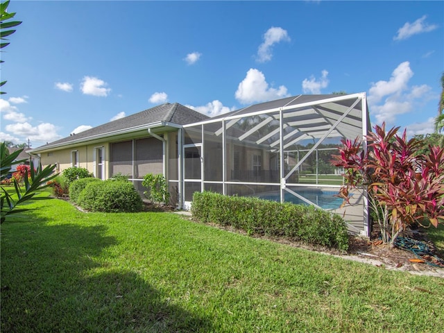 rear view of property featuring a yard and glass enclosure