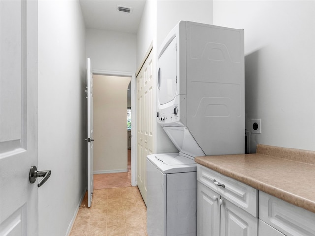 laundry area featuring cabinets, light tile patterned floors, and stacked washer and dryer