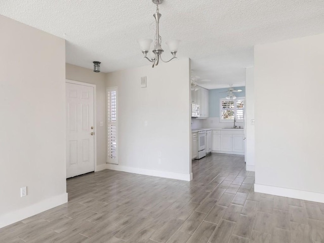 unfurnished dining area featuring ceiling fan with notable chandelier, a textured ceiling, light hardwood / wood-style floors, and sink