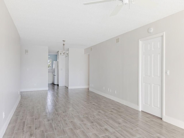 empty room with ceiling fan with notable chandelier and light wood-type flooring