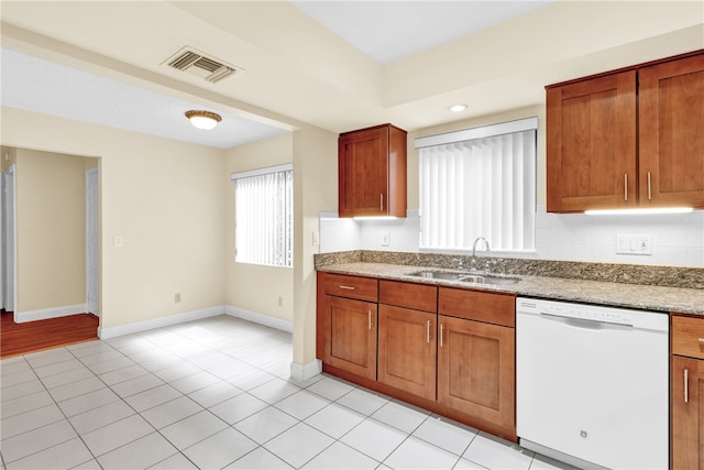 kitchen with dishwasher, sink, tasteful backsplash, light tile patterned flooring, and light stone countertops