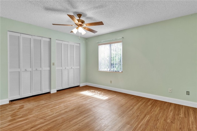 unfurnished bedroom featuring a textured ceiling, two closets, ceiling fan, and light hardwood / wood-style flooring