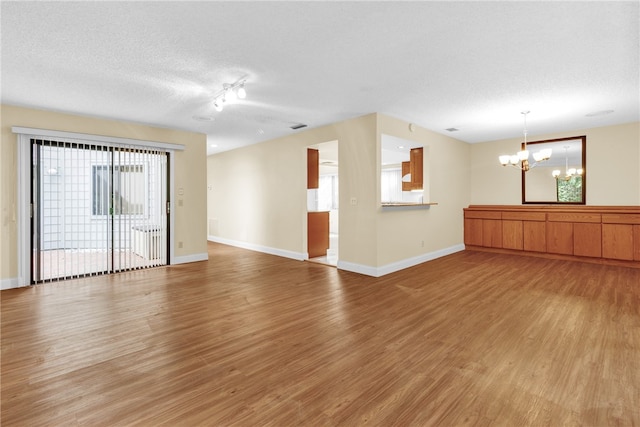 spare room featuring light wood-type flooring, a chandelier, and a textured ceiling