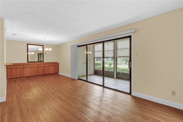 unfurnished room with an inviting chandelier, light hardwood / wood-style floors, and a textured ceiling