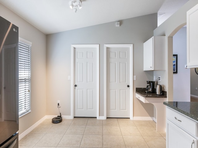 interior space with dark stone countertops, white cabinetry, vaulted ceiling, and light tile patterned flooring