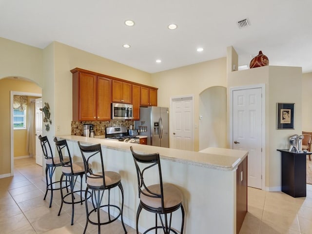 kitchen with light tile patterned floors, a breakfast bar, appliances with stainless steel finishes, decorative backsplash, and kitchen peninsula