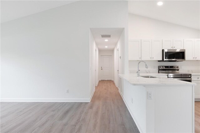 kitchen featuring white cabinets, sink, vaulted ceiling, light wood-type flooring, and appliances with stainless steel finishes