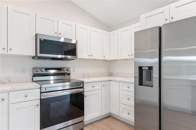 kitchen featuring stainless steel appliances, vaulted ceiling, and white cabinetry