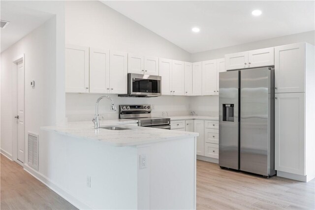 kitchen with sink, white cabinetry, stainless steel appliances, and vaulted ceiling