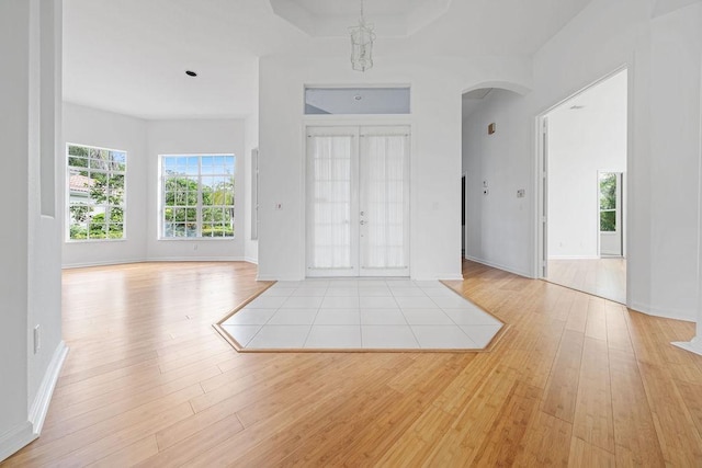 entrance foyer with french doors, light hardwood / wood-style floors, and a raised ceiling