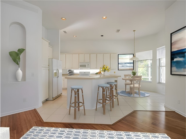 kitchen with white appliances, light tile patterned floors, a kitchen island, hanging light fixtures, and a breakfast bar area