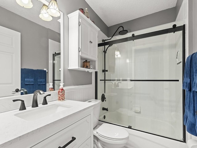 full bath featuring bath / shower combo with glass door, toilet, vanity, a textured ceiling, and a wainscoted wall