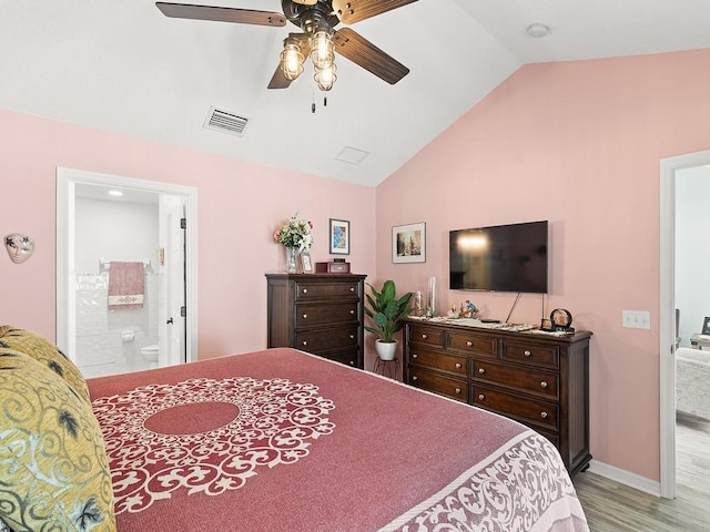 bedroom featuring vaulted ceiling, wood finished floors, baseboards, ensuite bath, and ceiling fan