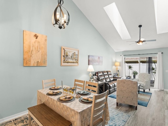 dining room with high vaulted ceiling, a skylight, wood finished floors, a ceiling fan, and baseboards