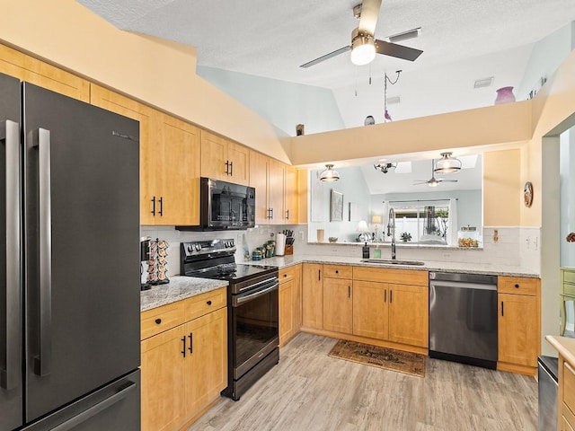kitchen featuring stainless steel appliances, ceiling fan, a sink, vaulted ceiling, and light wood-style flooring