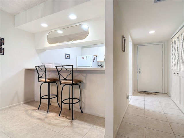 kitchen featuring light tile patterned flooring, a kitchen bar, and white fridge