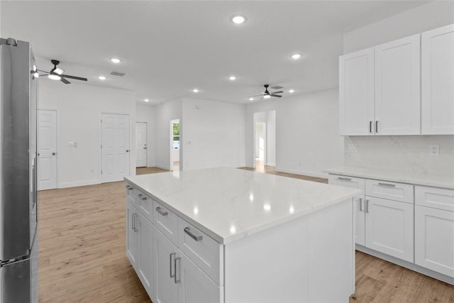 kitchen with stainless steel refrigerator, ceiling fan, light hardwood / wood-style floors, white cabinets, and a kitchen island