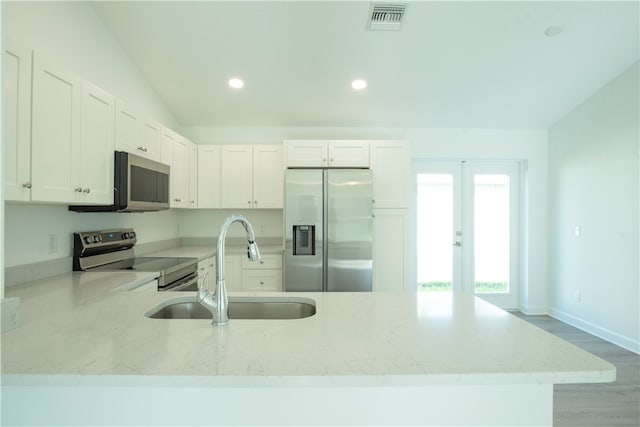 kitchen with stainless steel appliances, white cabinetry, light stone countertops, lofted ceiling, and light hardwood / wood-style flooring