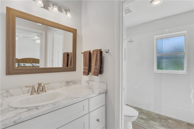 bathroom with ceiling fan, vanity, toilet, and tiled shower