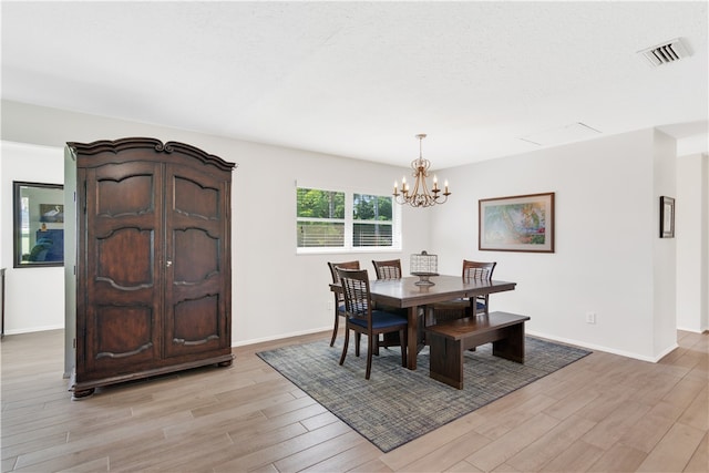 dining space with a textured ceiling, light wood-type flooring, and a chandelier