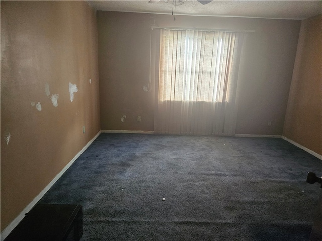 empty room with a textured ceiling, ceiling fan, and dark carpet