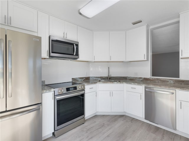 kitchen featuring light wood-type flooring, appliances with stainless steel finishes, decorative backsplash, and white cabinets