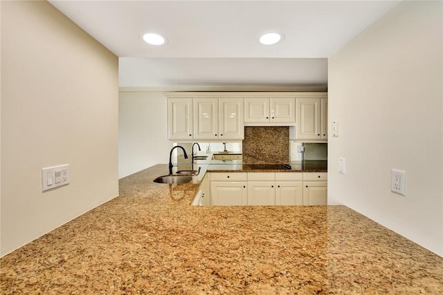 kitchen featuring backsplash, stone counters, black electric stovetop, kitchen peninsula, and sink