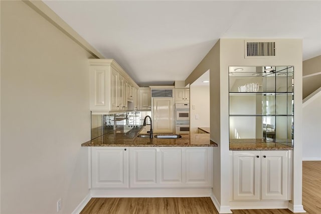 kitchen with kitchen peninsula, light wood-type flooring, dark stone counters, white cabinets, and sink