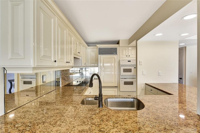 kitchen featuring kitchen peninsula, double oven, stone countertops, and sink