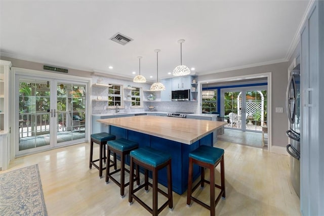 kitchen with appliances with stainless steel finishes, pendant lighting, white cabinets, french doors, and a breakfast bar area