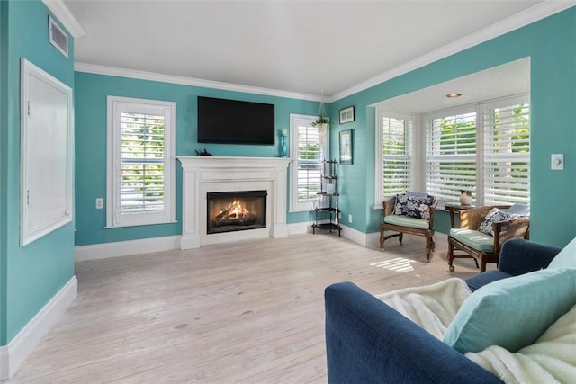 living area featuring crown molding, a lit fireplace, baseboards, plenty of natural light, and light wood-type flooring