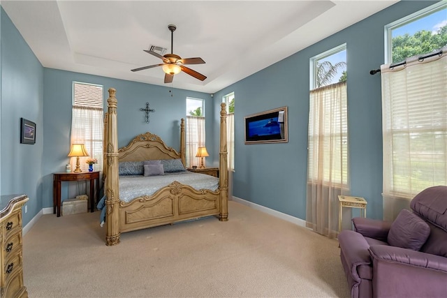 carpeted bedroom with a raised ceiling and ceiling fan