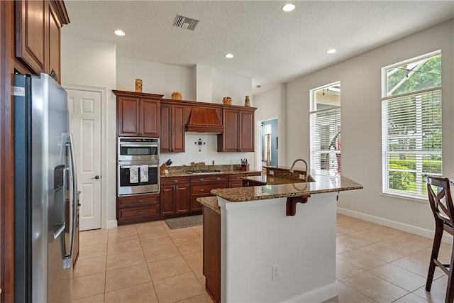 kitchen featuring appliances with stainless steel finishes, a breakfast bar, light tile patterned floors, and dark stone countertops