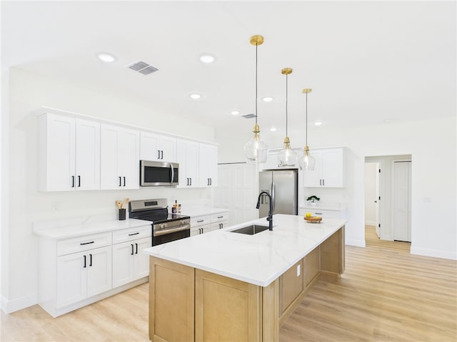 kitchen with visible vents, a sink, light wood-type flooring, appliances with stainless steel finishes, and a large island with sink