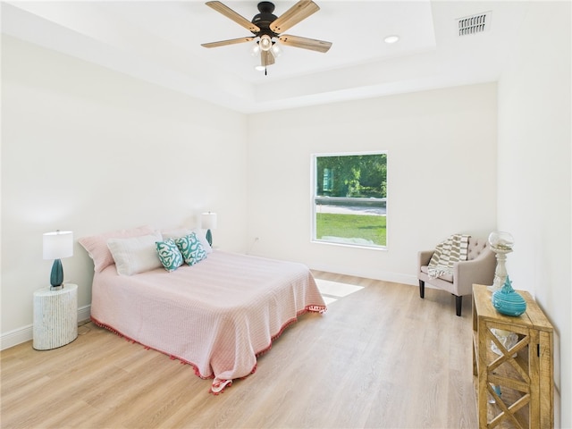 bedroom featuring light wood-style flooring, a raised ceiling, baseboards, and visible vents