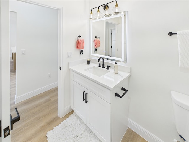half bathroom featuring toilet, wood finished floors, vanity, and baseboards