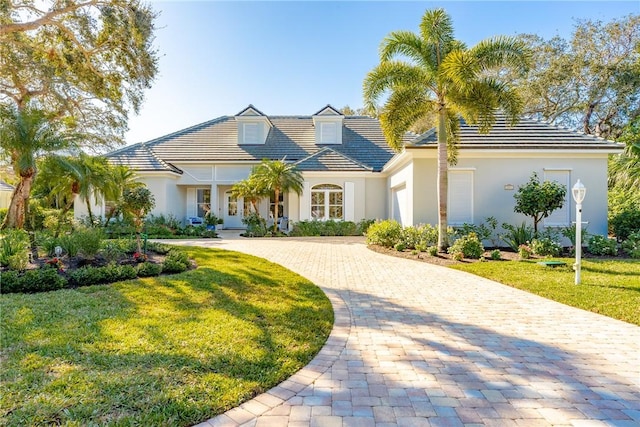 view of front of property with a tiled roof, a front lawn, decorative driveway, and stucco siding