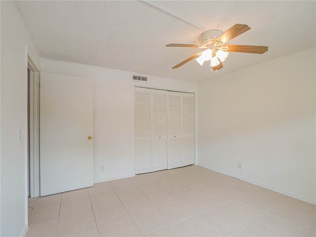 unfurnished bedroom featuring light tile patterned flooring, a closet, a textured ceiling, and ceiling fan