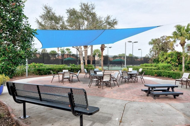 view of property's community with a tennis court, outdoor dining area, and fence