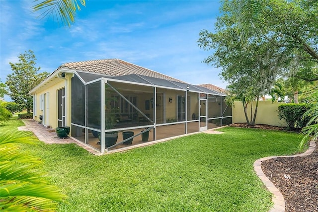 back of house with a lawn, a lanai, a tiled roof, and stucco siding