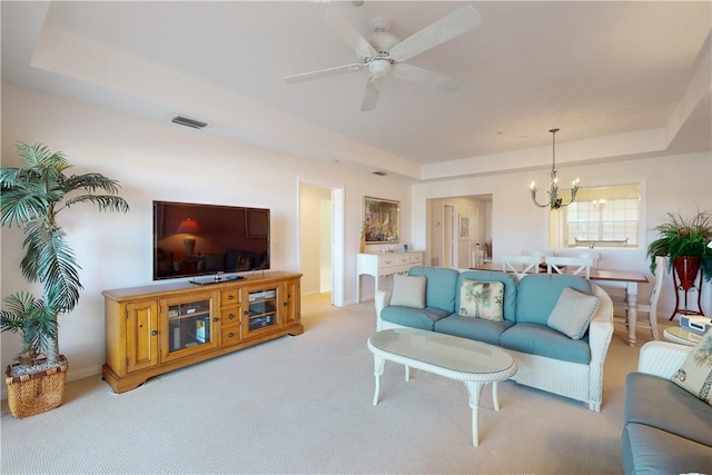 carpeted living room featuring a raised ceiling and ceiling fan with notable chandelier