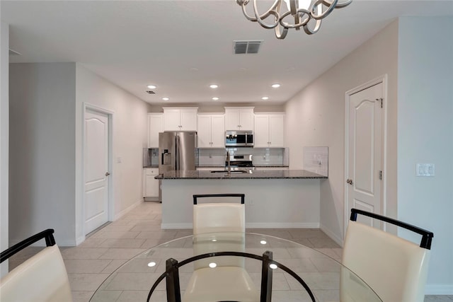 kitchen featuring stainless steel appliances, a sink, visible vents, tasteful backsplash, and dark stone countertops