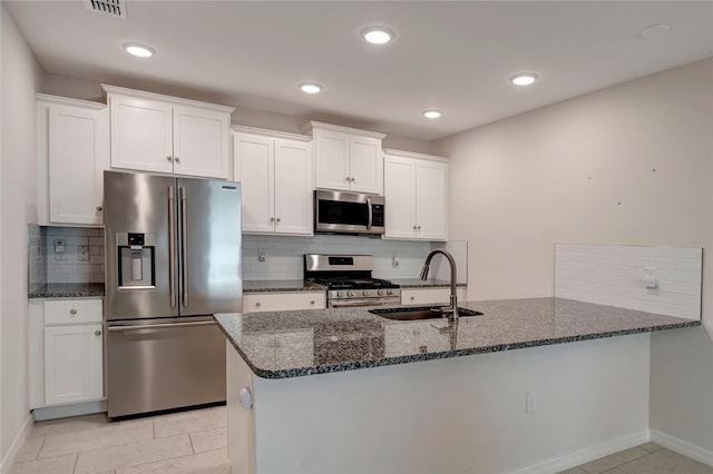 kitchen with decorative backsplash, white cabinets, appliances with stainless steel finishes, dark stone countertops, and a sink