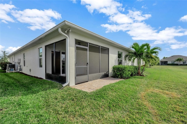 back of property with a sunroom, stucco siding, a lawn, and central AC unit